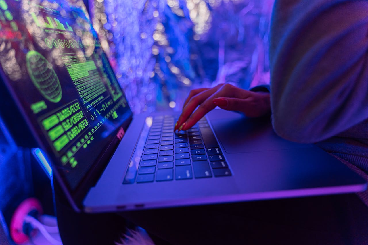 about-bg Close-up of hands typing on a laptop displaying cybersecurity graphics, illuminated by purple light.
