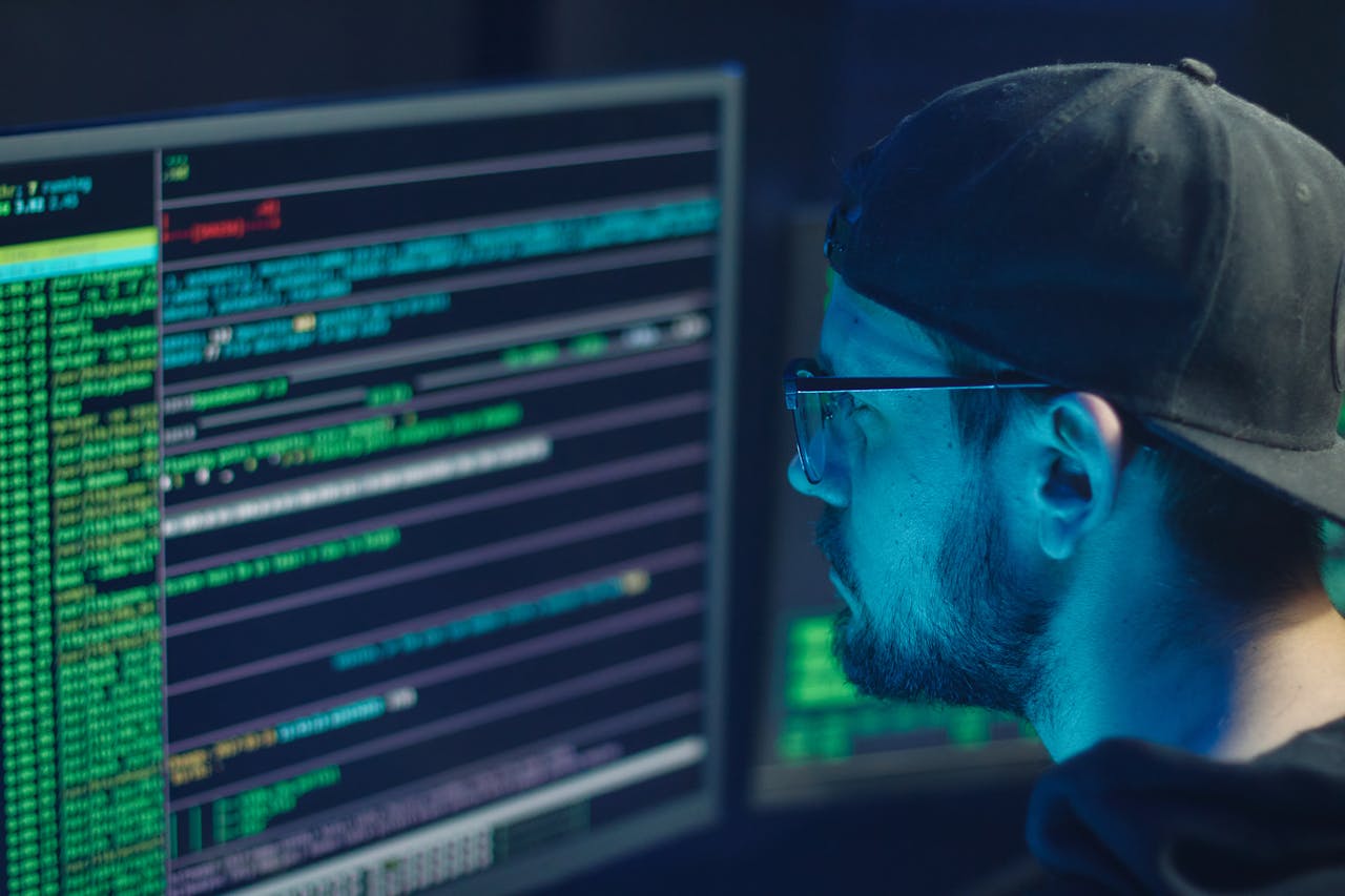 services-03 A cybersecurity expert inspecting lines of code on multiple monitors in a dimly lit office.