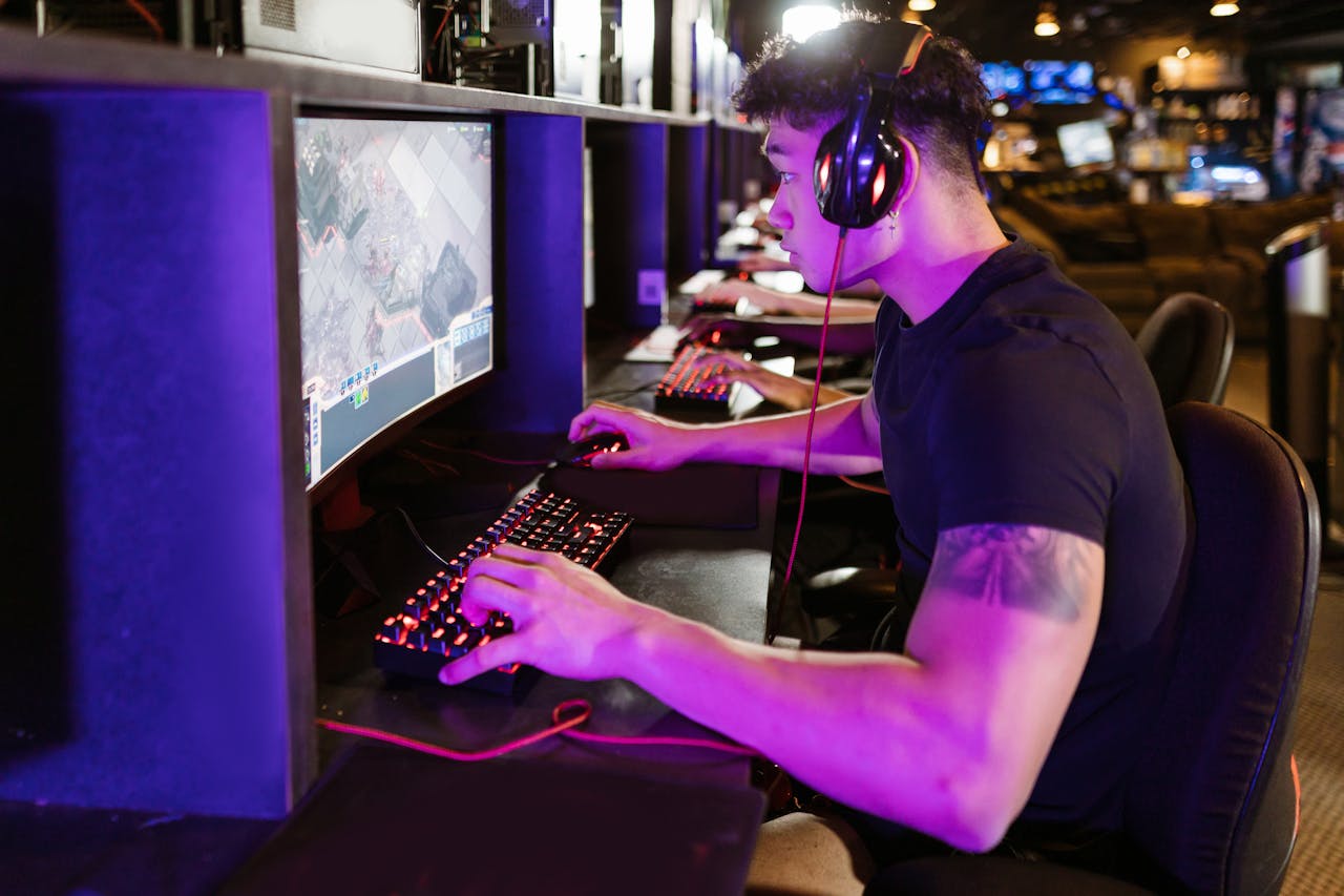 services-02 A focused gamer plays on a high-performance PC in a modern cyber café setting under purple lighting.